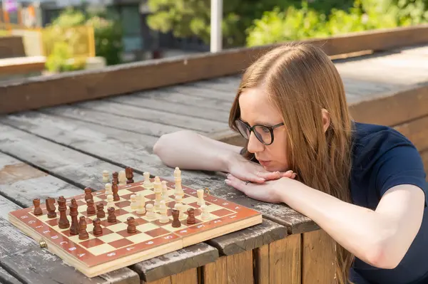 Beyaz kadın dışarıda satranç oynuyor.