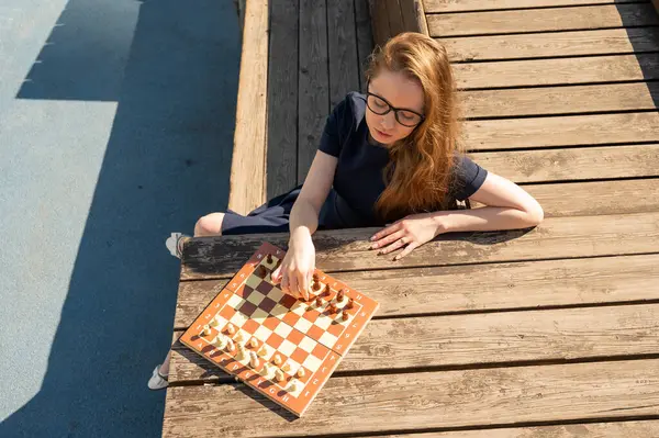 Beyaz kadın dışarıda satranç oynuyor.