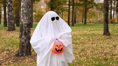 Beyaz çarşaflı bir kadın elinde balkabağı şeklinde bir sepet tutuyor ve sonbahar ormanından şeker istiyor. Cadılar Bayramı kostümü