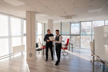 İki beyaz adam dizüstü bilgisayara bakıyor ve iş tartışıyorlar.