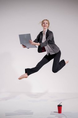 Beyaz arka planda dizüstü bilgisayarla atlayan takım elbiseli çıplak ayaklı balerin.