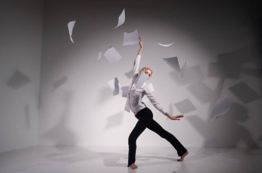 Takım elbiseli zarif bir balerin belgeleri fırlatır. İş kadını beyaz arka planda yalınayak dans ediyor..