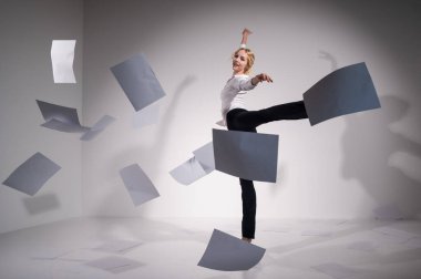 Takım elbiseli zarif bir balerin belgeleri fırlatır. İş kadını beyaz arka planda yalınayak dans ediyor..