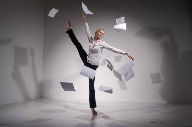 Takım elbiseli zarif bir balerin belgeleri fırlatır. İş kadını beyaz arka planda yalınayak dans ediyor..