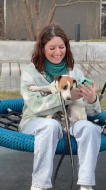 Beyaz kadın Jack Russell Terrier 'ını gezdirirken akıllı telefon kullanıyor.