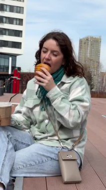 Beyaz kadın kruvasan yiyor ve dışarıda kahve içiyor.