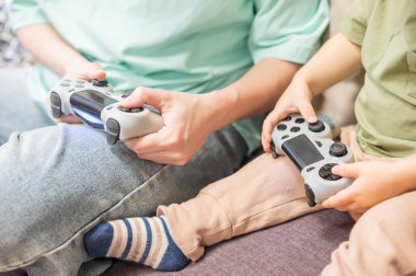 Beyaz kadın küçük oğluna konsol oynamayı öğretiyor. Oyun kolu ellerinde.