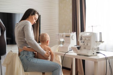 Genç bir kadın evde dikiş dikiyor ve kucağında küçük bir çocuk tutuyor. Annesi küçük oğluna dikiş makinesi dikmeyi öğretiyor..