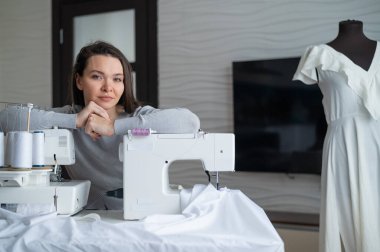 Beyaz kadın evde bir elbise dikiyor. Bir terzinin çalışma alanı.