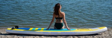 SUP panosunda poz veren beyaz bir kadın. Yaz sporu