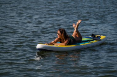 SUP panosunda poz veren beyaz bir kadın. Yaz sporu