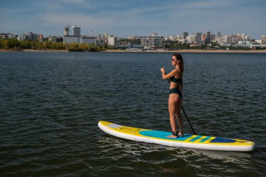 Gölde SUP sörf tahtası süren beyaz bir kadın. Yaz sporu