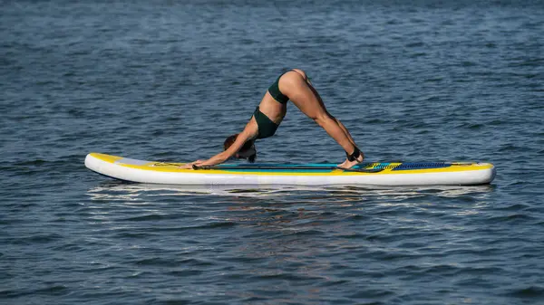 Beyaz kadın SUP panosunda yoga yapıyor.