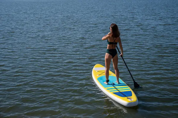 Gölde SUP sörf tahtası süren beyaz bir kadın. Yaz sporu