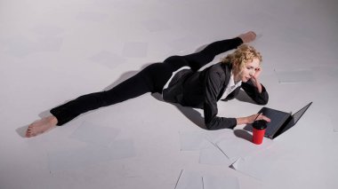 İş elbisesi giymiş bir balerin orta sicimle oturur, dizüstü bilgisayarda çalışır ve kahve içer. Bilgisayar başında esnek bir kadın çalışıyor..