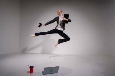 Beyaz arka planda dizüstü bilgisayarla atlayan takım elbiseli çıplak ayaklı balerin.