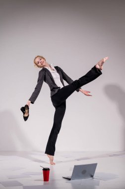 Beyaz arka planda iş elbisesiyle dans eden çıplak ayaklı balerin.