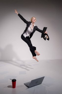 Beyaz arka planda dizüstü bilgisayarla atlayan takım elbiseli çıplak ayaklı balerin.