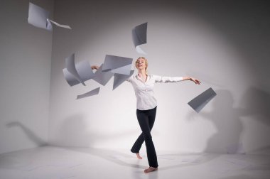 Takım elbiseli zarif bir balerin belgeleri fırlatır. İş kadını beyaz arka planda yalınayak dans ediyor..