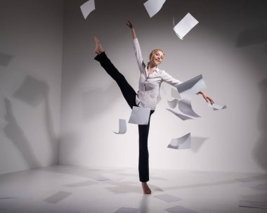 Takım elbiseli zarif bir balerin belgeleri fırlatır. İş kadını beyaz arka planda yalınayak dans ediyor..