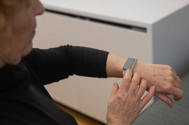 Kafkasyalı yaşlı bir kadın akıllı saate bakıyor. Ellerin yakın çekimi