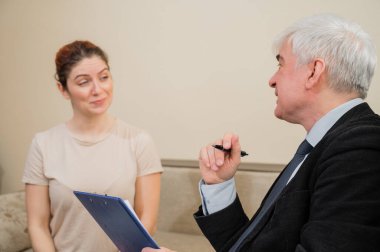 Kadın hastayla seans halinde olan beyaz saçlı erkek psikoterapist. Psikolog randevusunda gülümseyen beyaz kadın.