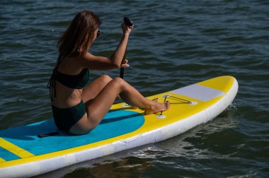 Gölde SUP sörf tahtası süren beyaz bir kadın. Yaz sporu