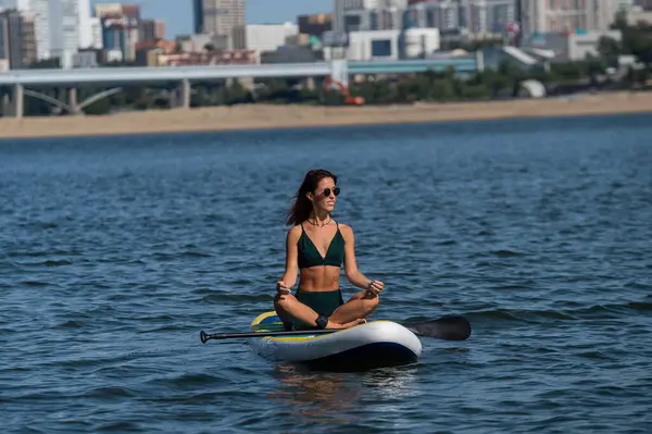 Beyaz kadın SUP panosunda yoga yapıyor.