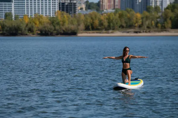 Beyaz kadın SUP panosunda yoga yapıyor.