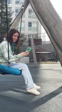 Beyaz kadın salıncakta sallanıyor ve akıllı telefon kullanıyor.