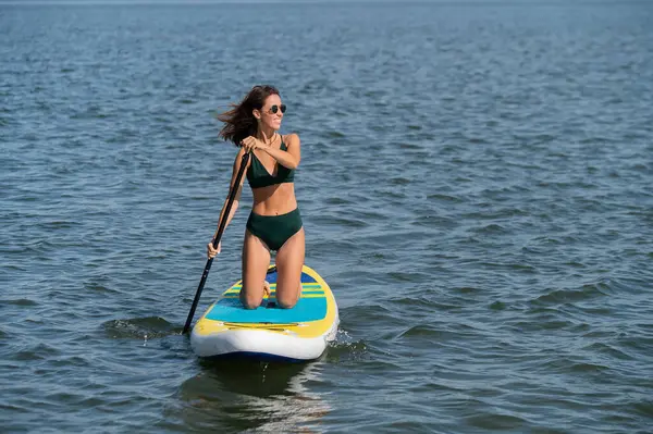 Gölde SUP sörf tahtası süren beyaz bir kadın. Yaz sporu