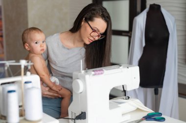 Genç bir kadın evde dikiş dikiyor ve kucağında küçük bir çocuk tutuyor. Annesi küçük oğluna dikiş makinesi dikmeyi öğretiyor..