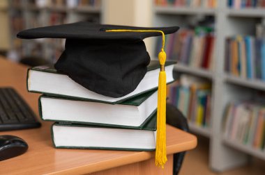 Kütüphanedeki bir yığın kitabın mezuniyet şapkası.