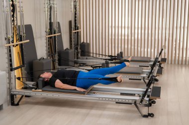 Aşırı kilolu beyaz kadın bir reformcu üzerinde pilates egzersizi yapıyor.