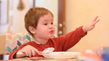 Şirin bir çocuk tek başına yulaf lapası yiyor.