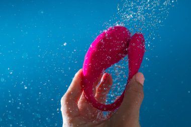 Duşta pembe vibratörü yıkayan kadın. Mavi arka planda su geçirmez seks oyuncağı