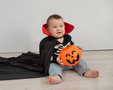 Beyaz arka planda şeker sepeti tutan Dracula Cadılar Bayramı kostümlü beyaz tatlı çocuk.
