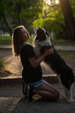 Beyaz bir kadın parkta yürürken köpeğine sarılıyor.