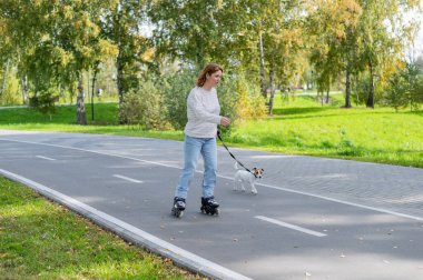 Beyaz kadın, Jack Russell Terrier köpeğiyle parkta paten kayıyor.