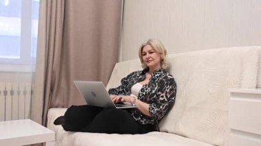 Kanepede otururken laptop kullanan olgun bir kadın.