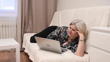 Kanepede yatarken laptop kullanan olgun bir kadın.