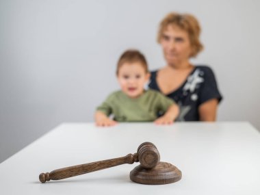 Yaşlı bir kadın jürinin arkasında bir çocuk tutuyor.