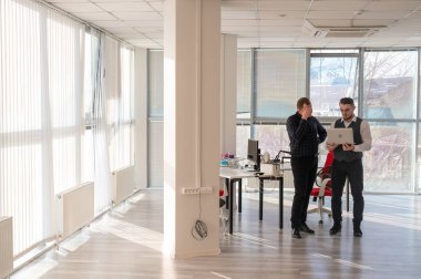 İki beyaz adam dizüstü bilgisayara bakıyor ve iş tartışıyorlar.