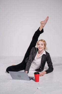 İş elbisesi giymiş çıplak ayaklı balerin dizüstü bilgisayara poz veriyor ve kahve içiyor. Bilgisayar başında esnek bir kadın çalışıyor..