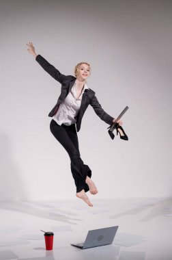 Beyaz arka planda dizüstü bilgisayarla atlayan takım elbiseli çıplak ayaklı balerin.