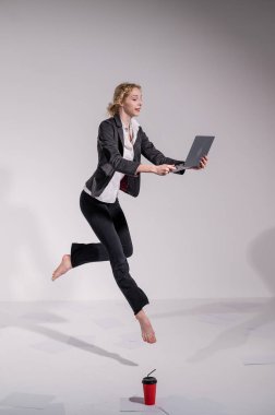 Beyaz arka planda dizüstü bilgisayarla atlayan takım elbiseli çıplak ayaklı balerin.