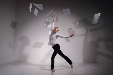 Takım elbiseli zarif bir balerin belgeleri fırlatır. İş kadını beyaz arka planda yalınayak dans ediyor..