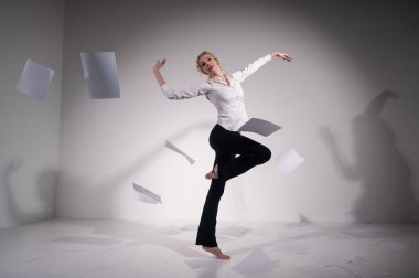 Takım elbiseli zarif bir balerin belgeleri fırlatır. İş kadını beyaz arka planda yalınayak dans ediyor..