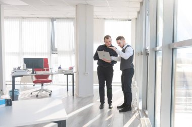 İki beyaz adam dizüstü bilgisayara bakıyor ve iş tartışıyorlar.