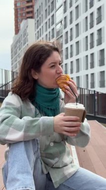 Beyaz kadın kruvasan yiyor ve dışarıda kahve içiyor.